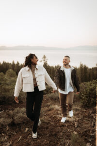 Engaged couple holds hands, soaking in the sunrise at a scenic overlook in Lake Tahoe